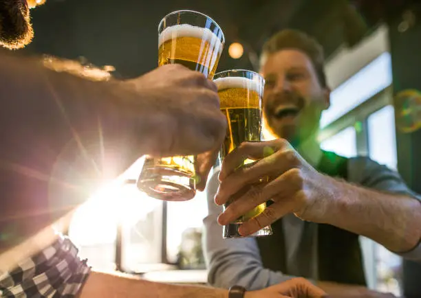 Close up of happy men having fun while toasting with beer in a bar.