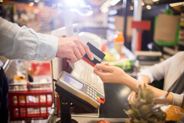 Man Paying with Credit Card in Supermarket Side view close up of unrecognizable customer handing credit card to cashier paying via bank terminal at grocery store cashier stock pictures, royalty-free photos & images