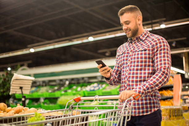 istock Handsome Man Holding Smartphone in Supermarket 876907484