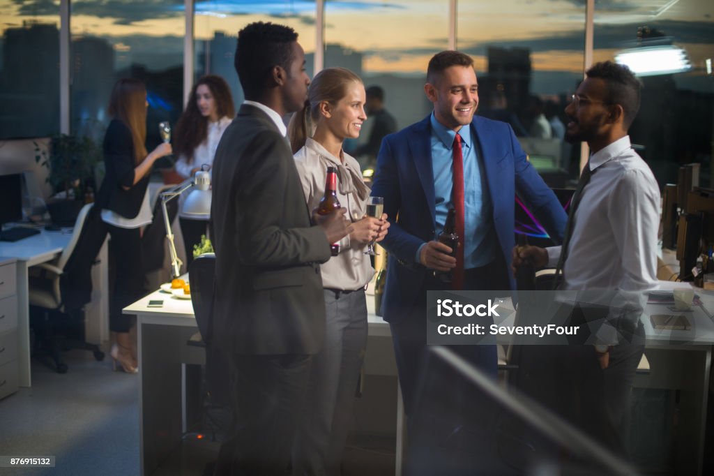 Business party in office Young stylish office workers standing in office with alcoholic beverages, talking and smiling Business Stock Photo