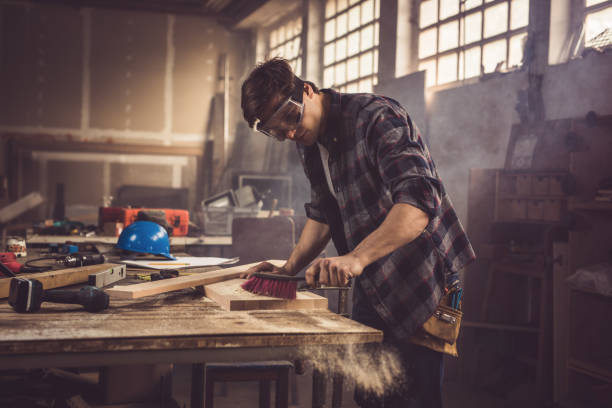 istock Male carpenter cleaning a wood from sawdust in a workshop. 876931094