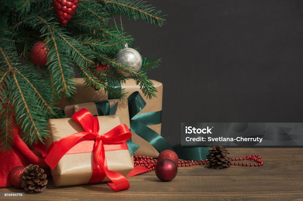 Weihnachten Urlaub Hintergrund. Geschenke mit einem roten Band, Santas Hut und Dekor unter einem Baum auf einem Holzbrett. - Lizenzfrei Weihnachtsbaum Stock-Foto