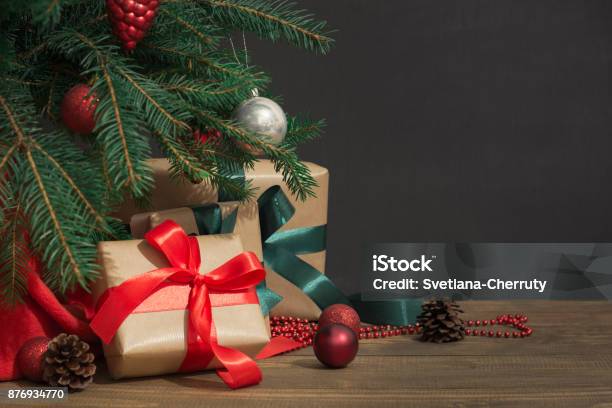 Weihnachten Urlaub Hintergrund Geschenke Mit Einem Roten Band Santas Hut Und Dekor Unter Einem Baum Auf Einem Holzbrett Stockfoto und mehr Bilder von Weihnachtsbaum