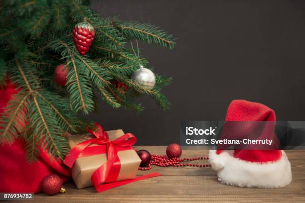 Weihnachten Urlaub Hintergrund Geschenke Mit Einem Roten Band Santas Hut Und Dekor Unter Einem Baum Auf Einem Holzbrett Stockfoto und mehr Bilder von Unterhalb