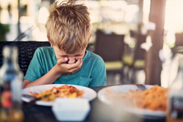 Little boy fussy eater in restaurant. The boy doesnt want to eat and he is even going to throw up even looking at his plate.\n