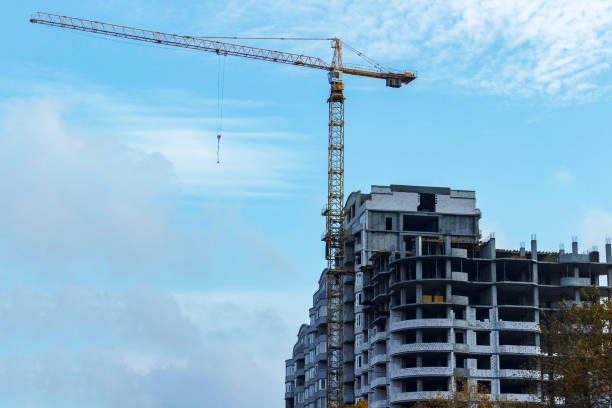 istock unfinished building construction and building cranes against clear blue sky background 876956712
