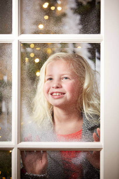 istock Girl looking through snowy window at Christmas. 876975586