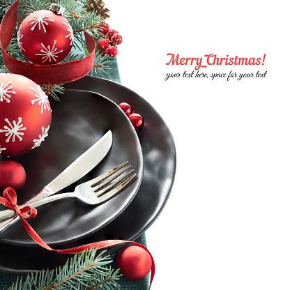 Christmas menu concept with black plates and cutlery decorated with Christmas tree twigs and baubles, isolated on white, text space