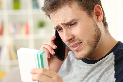 Worried man calling doctor on phone asking about medicines information sitting on a couch at home