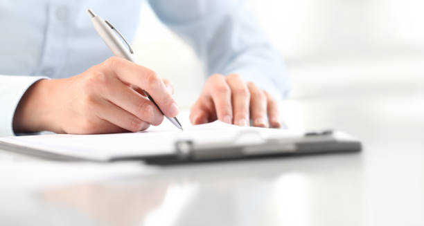 Woman's hands writing on sheet of paper in a clipboard with pen isolated on desk Woman's hands writing on sheet of paper in a clipboard with pen isolated on desk registration form photos stock pictures, royalty-free photos & images