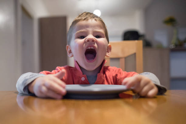 Child in the kitchen during the day eating pasta at the table, looking at camera. Healthy food. Healthy meal.