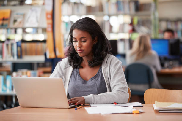 mature female student travaillant sur ordinateur portable dans la bibliothèque du collège - adult student women mature adult library photos et images de collection