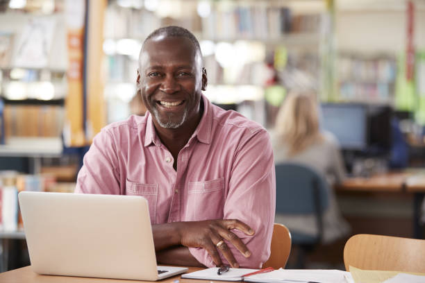 ritratto di studente maschio maturo che usa laptop in libreria - mature adult men male african descent foto e immagini stock