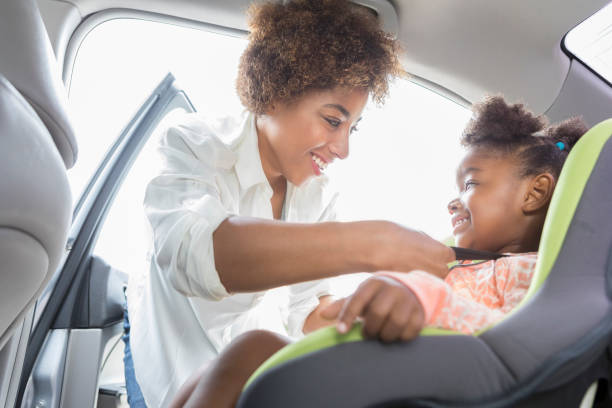 istock Caring mom carefully straps daughter into car seat 877029694