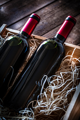 High angle view of a wooden box with two wine bottles inside it shot on rustic wooden table. Predominant colors are brown and red. Low key DSRL studio photo taken with Canon EOS 5D Mk II and Canon EF 100mm f/2.8L Macro IS USM