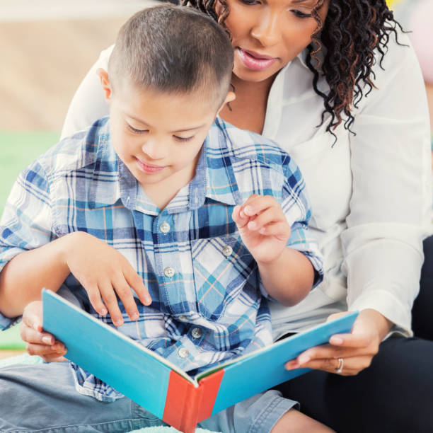 istock Caring preschool teacher reads book with boy with differing abilities 877030744