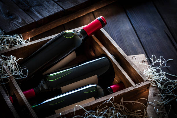 Red wine bottles packed in a wooden box shot rustic wooden table High angle view of a wooden box with three red wine bottles shot on rustic wooden table. The labels on the bottles are blank so you can put any design on them. Predominant color is brown. crate photos stock pictures, royalty-free photos & images