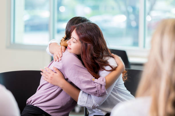 istock Young woman embraces friend during support group meeting 877031388