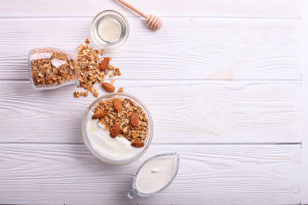 granola superfood con mandorle e anacardi, frutta secca, ciliegia di uvetta nel gufo di vetro con latte e yogurt greco sul tavolo in legno bianco, vista dall'alto - avena cereali da colazione foto e immagini stock