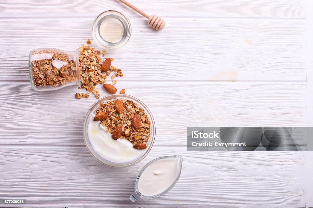 Granola superfood with almond and cashew nuts, dry fruits, raisins cherry in the glass bawl with milk and greek yogurt on the white wood table, top view healthy nutritious fitness snacks Yogurt Stock Photo