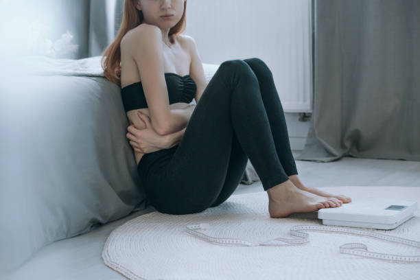 Sick girl with stomach pain Close-up of young sick girl with stomach pain sitting on white carpet with foot on balance bulimia stock pictures, royalty-free photos & images