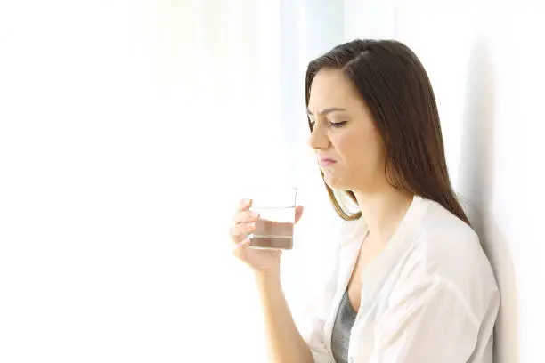 Disgusted woman drinking water with bad taste isolated on white at side