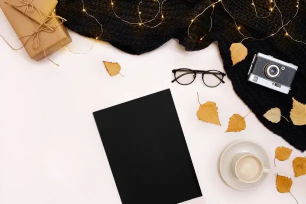 Photo of Romantic autumn mock up. Sheet of black paper, yellow and orange leaves, pencils, cup of cappuccino and old camera.Top view. Flat lay