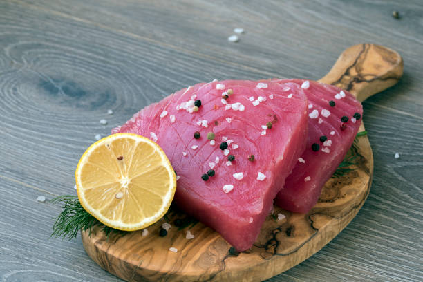 filetto di tonno crudo con aneto, limone e peperoni in tagliere di olive - tuna steak fillet food plate foto e immagini stock