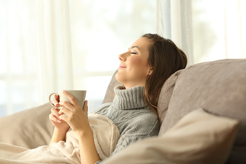 Woman relaxing holding a coffee mug sitting on a sofa in the living room in a house interior
