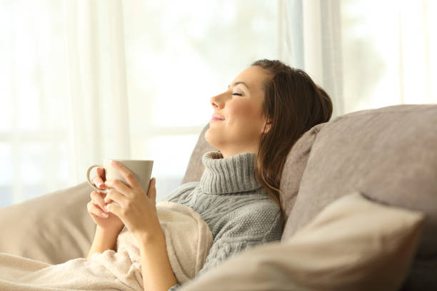 Woman relaxing at home holding a coffee mug Woman relaxing holding a coffee mug sitting on a sofa in the living room in a house interior serene people stock pictures, royalty-free photos & images