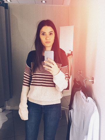 Young woman trying out clothes in a fitting room and photographing herself in a mirror // mobile stock photo made with iPhone 6s