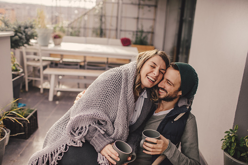 Photo of a young couple taking a few minutes off to relax and drink coffee on their balcony, on a beautiful autumn day