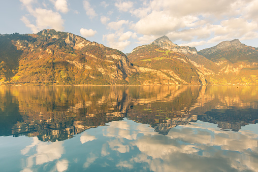 Autumn. Mountains and clouds are reflected in the water of Lake Lucerne. Canton of Uri, Switzerland.
