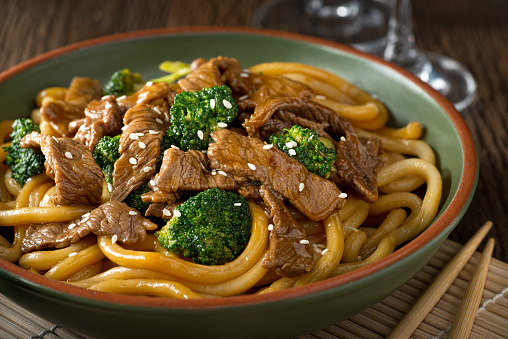 A bowl of delicious beef teriyaki with broccoli, udon noodles and sesame seed garnish.