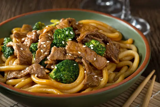 A bowl of delicious beef teriyaki with broccoli, udon noodles and sesame seed garnish.