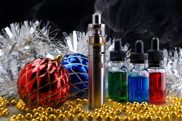 istock Electronic cigarette with vape liquids within vapor and christmas decorations on black background 877114932