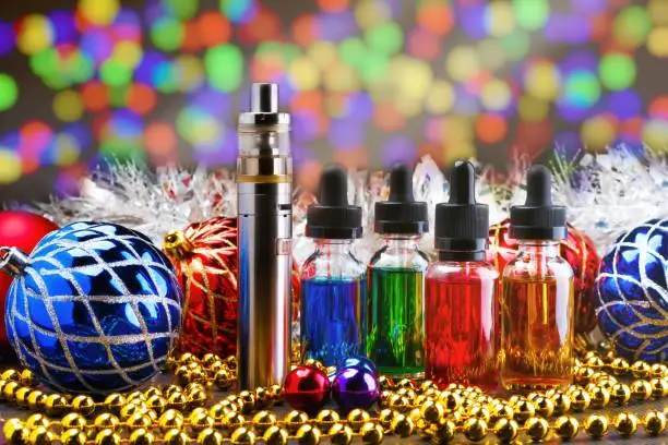 Electronic cigarette or vaping device, assorted vape liquids and christmas decorations on colourful bokeh lights background