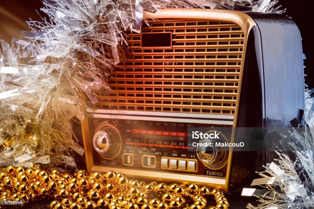 radio receiver in retro style with christmas decorations and light beams on black background modern retro styled radio with audio player and colored christmas decorations on black background. Toned light effects Christmas Stock Photo