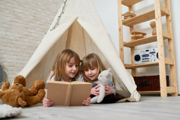 istock Pretty sisters reading book in teepee tent 877122808