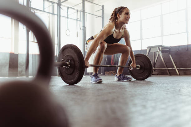 Woman lifting a barbell at the gym Young woman lifting a barbell at the gym. Fit female athlete exercising with heavy weights at cross training gym. powerlifting stock pictures, royalty-free photos & images