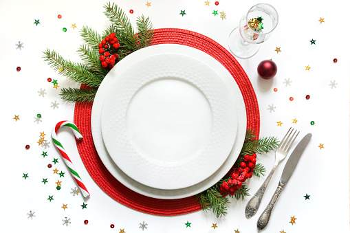 Christmas table setting with vintage dishware, silverware and red decorations on white background. Top view.