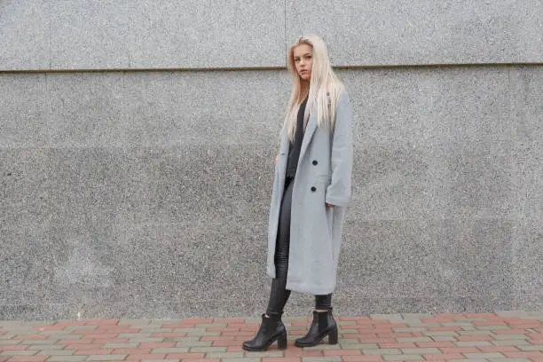 Photo of Fashion style young elegant woman in gray fur coat walking at city street.