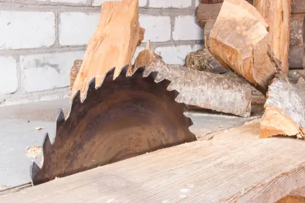 Circular saw for wood and tree trunks in sawmill close up. On table next to saw are firewood for heating stoves, fireplaces and campfires. Processing of wood for boards or other building materials