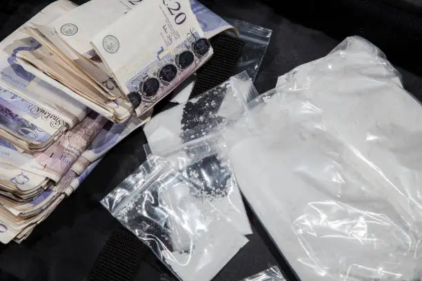 UK drug crime. Cash and cocaine. A dealers cash from selling illegal drugs. White powder in bags with substantial amount of money.