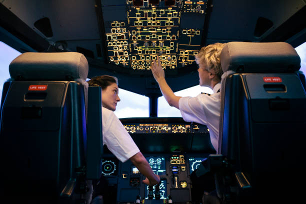 trainee pilot adjusting switches while instructor watches on during simulator session - airplane cockpit taking off pilot imagens e fotografias de stock