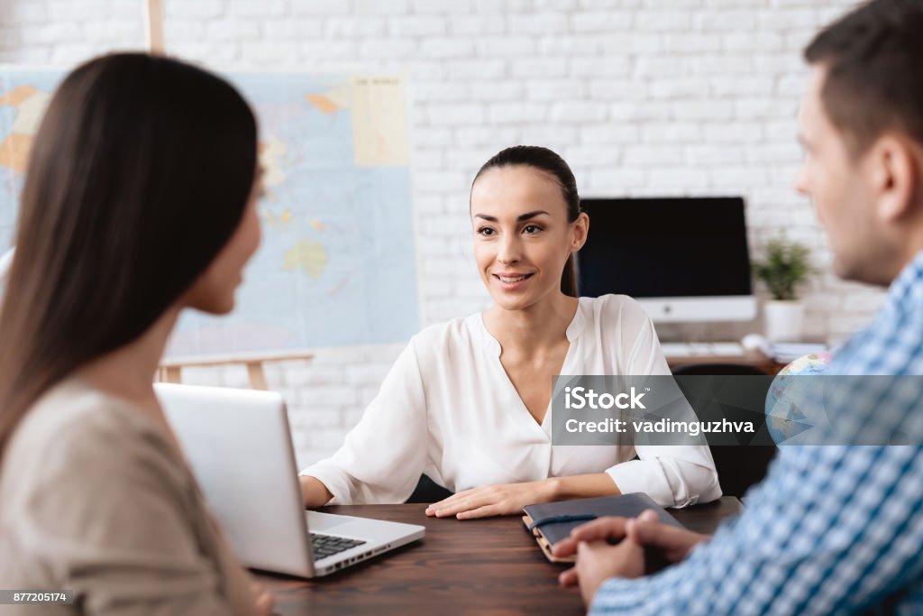 A young man and a woman came to the travel agency. A young man and a woman came to the travel agency. They want to go on a trip during their holidays. The girl agent offers them different countries. Travel Agency Stock Photo