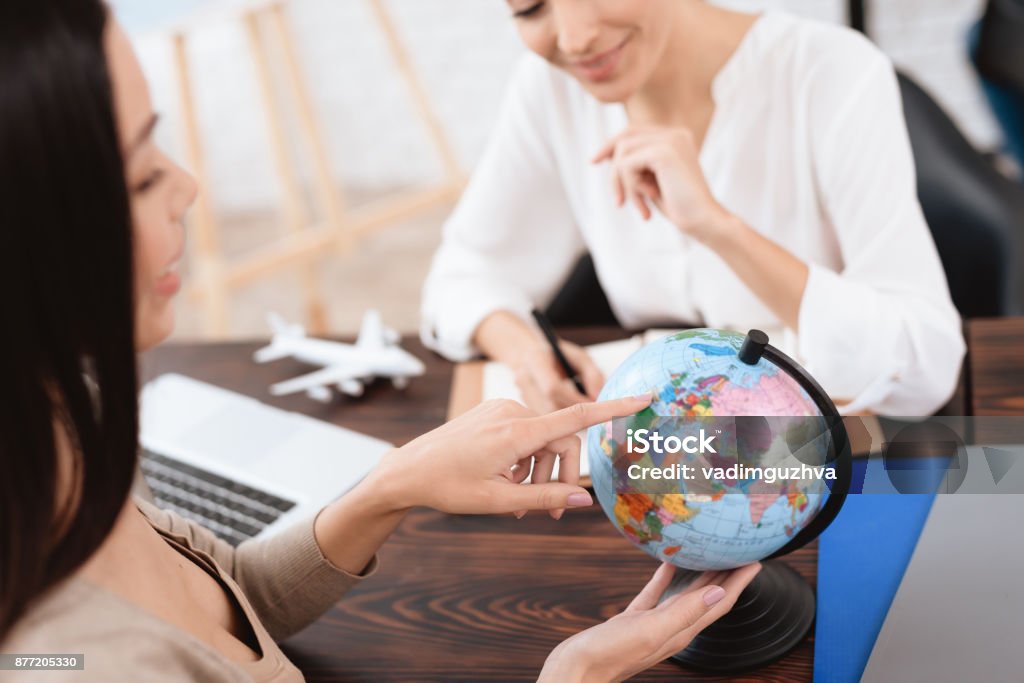 A young girl came to a travel agency. A young girl came to a travel agency. She wants to make journey. The travel agent helps her. Adult Stock Photo
