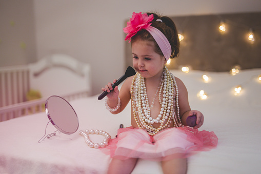 two and a half year old girl wants to be like her mother , so she is using mother jewelry and make up