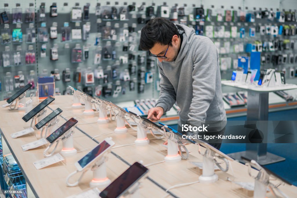 Smart male customer choosing smartphone Smart male customer choosing smartphone in the mobile phone shop. difficult decision. Various choice. He is smiling Store Stock Photo