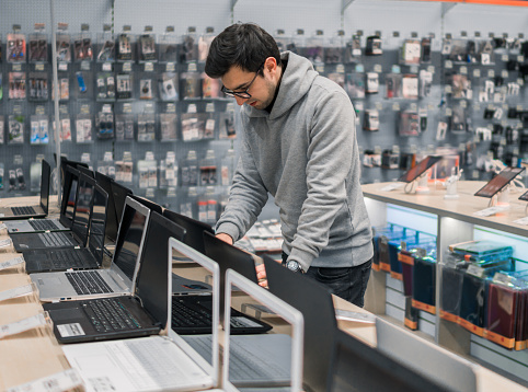 Smart modern male customer choosing laptop in the computer shop. difficult decision. He is opening notebook for checking.